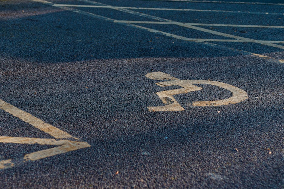 Close-up view of an outdoor parking area pavement featuring painted white parking space lines and a number '22' marked on the asphalt. The surface appears textured with small pebbles embedded in the black tarmac. In the background, part of a van parked on the street is visible, extending into the loading area, which is adjacent to a doorway leading into a property. The scene includes a section of the pavement designated for vehicle parking, with some alignment markings, and is situated on London Road, Thornton Heath. This setting is relevant to house removals and furniture transport, illustrating the environment where a Man with Van Thornton Heath operates during a home relocation process, assisting with loading and unloading in tight urban parking conditions.