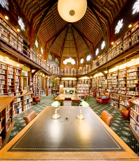 Interior view of a historic, multi-level library with ornate wooden beams and detailed woodwork. Tall, stained glass windows allow natural light to illuminate the space. Shelves filled with numerous hardcover books line the walls and extend to an upper balcony with a wooden railing. The ground floor features a few tables and chairs, suggesting a reading or study area. This setting, possibly within a heritage building, showcases the craftsmanship of traditional timber framing and serves as a backdrop for house removals or packing and moving services, such as those offered by Man with Van Thornton Heath, which may include relocation logistics and furniture transport within historic or residential properties.